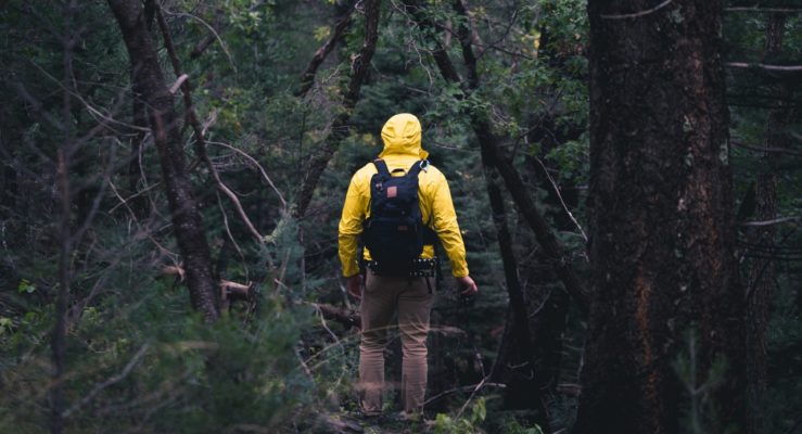 Man in gele regenjas en zwarte rugzak loopt in eeen donker bos